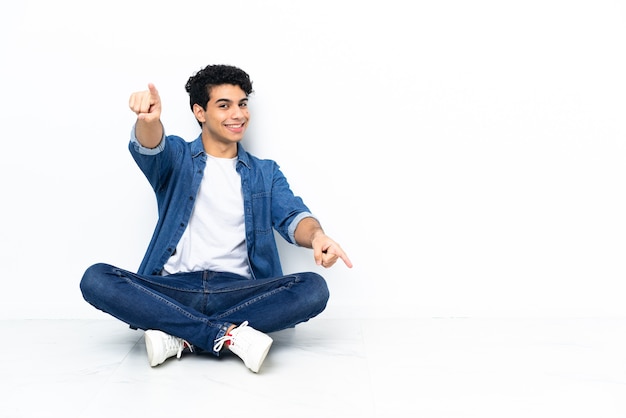 Venezuelan man sitting on the floor points finger at you while smiling