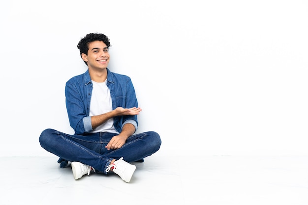 Venezuelan man sitting on the floor presenting an idea while looking smiling towards