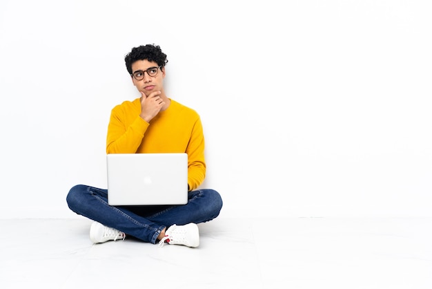 Venezuelan man sitting on the floor with laptop having doubts