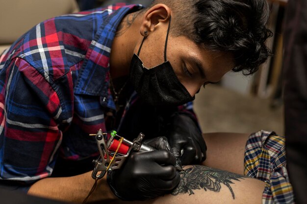 Venezuelan tattoo artist with mouth cover and black gloves performing a tattoo created by him Body art concept