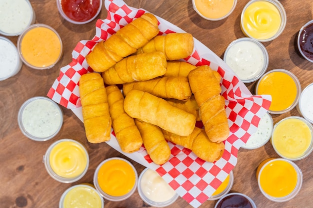 Photo venezuelan tequenos made of cheese with a lot of sauces around it on a wooden background.