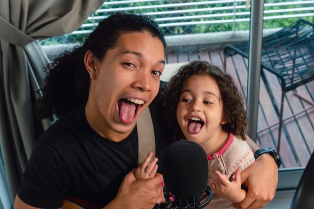 Venezuelan young father playing with his daughter sticking out his tongue looking at the camera