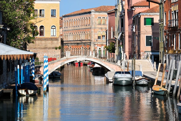 反射のある運河を渡る歩道橋のあるイタリアのヴェネツィア。古い家。ロマンチックな古い建築。