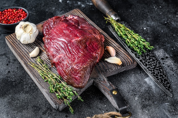 Venison raw deer meat on a cuuting board with herbs. Black table. Top view.