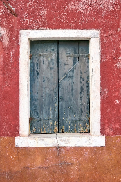 Venster met gesloten oud groen groen luik op rode muur. Italië, Venetië, Burano-eiland.