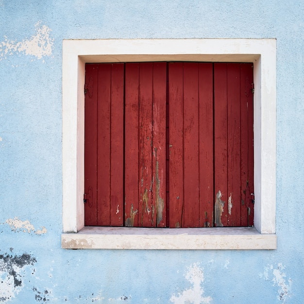 Venster met gesloten rood luik op blauwe muur. Italië, Venetië, Burano-eiland.