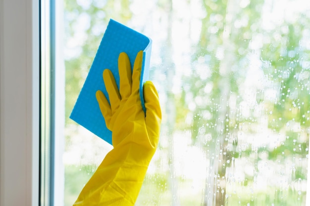 Vensterglas wassen. Een hand in een gele handschoen wast het raam met een blauwe lap