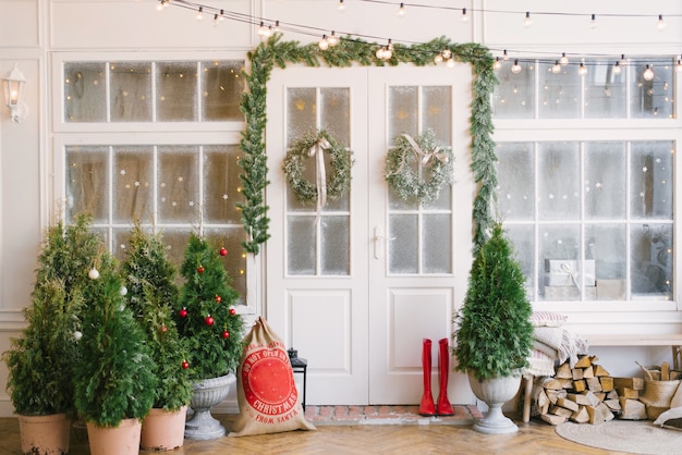 Veranda met een witte deur in kerstversiering en kerstbomen.