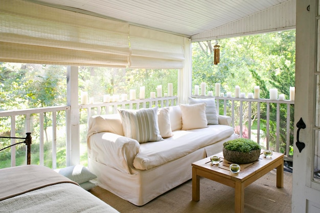 A verandah or shaded porch of a house in the woods with cream sofa and candles along the balustrade