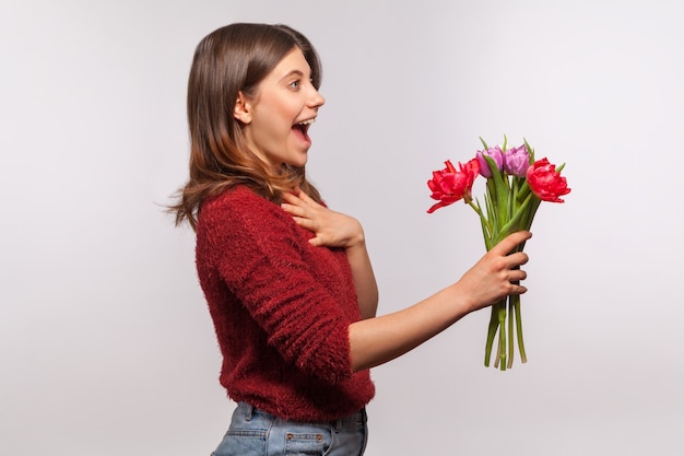 Verbaasd brunette meisje dat bloemenboeket geeft of felicitaties accepteert met de lentevakantie