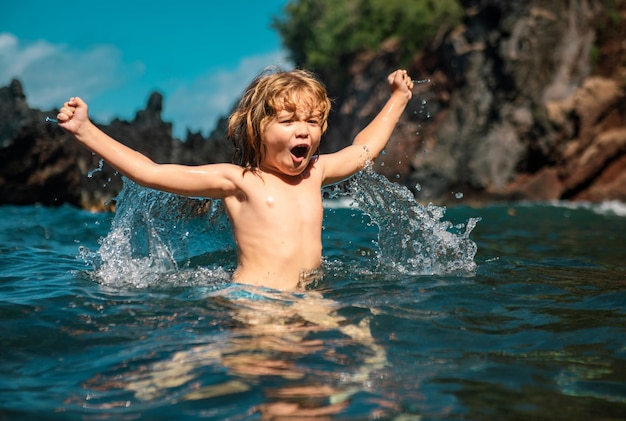 Verbaasd kind dat speelt en spettert in de zee, kind dat plezier heeft buiten zomervakantie en gezonde fa