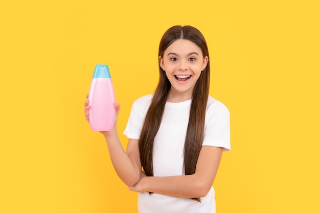 Verbaasd kind houdt de fles haarconditioner op gele schoonheid als achtergrond