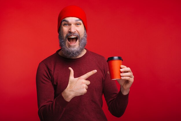 Verbaasd man met witte baard wijzend op rode kopje koffie