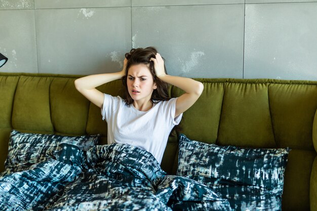 Verbaasd mooie jonge vrouw wakker in bed met geschokt gezicht emotie