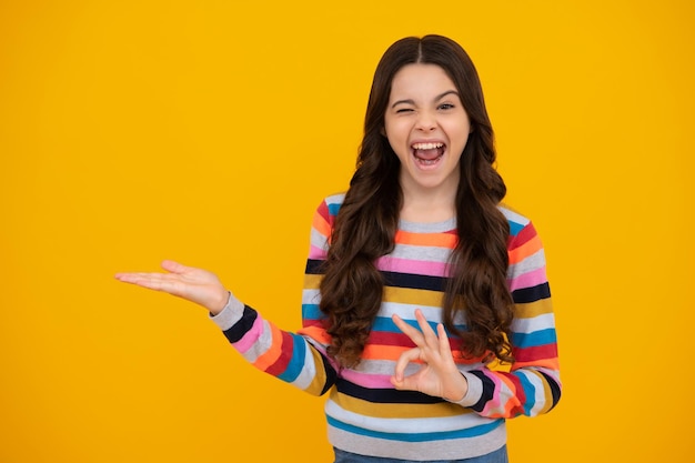 Verbaasd tiener portret van schattige tiener kind meisje wijzende hand tonen advertenties met kopie ruimte over gele achtergrond Opgewonden tiener meisje