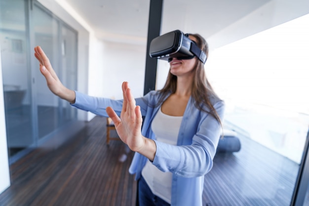 Verbaasd verrast jonge vrouw met een virtual reality-bril die de lucht aanraakt tijdens het vr-ervaringsspel thuis