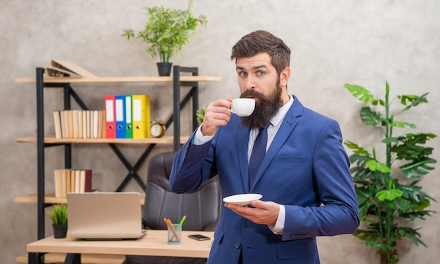 Verbaasde bebaarde zakenman die koffie drinkt op kantoor met kopieerruimte, professioneel.