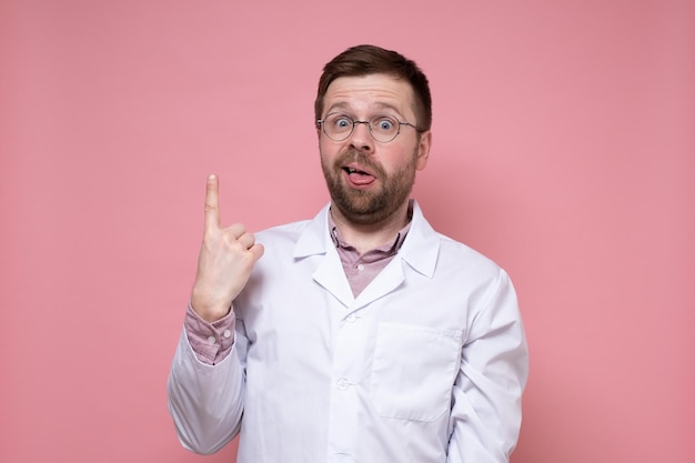 Verbaasde dokter met bril en een witte jas wijst omhoog met wijsvinger en maakt een domme grimas