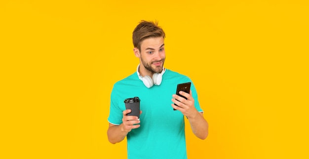 Verbaasde man houdt smartphone en koffiekopje vast op gele communicatie als achtergrond