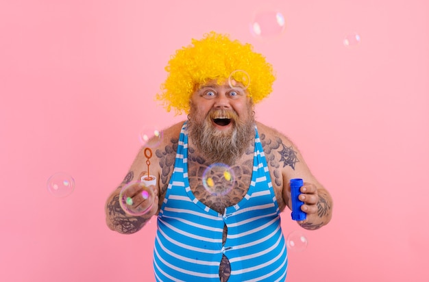 Verbaasde man met gele pruik in hoofd speelt met zeepbellen