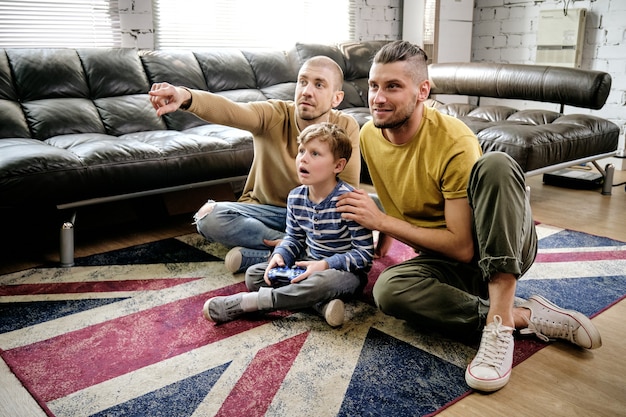 Verbaasde preteen jongen en twee jongens die op de grond zitten en thuis een nieuwe videogame spelen