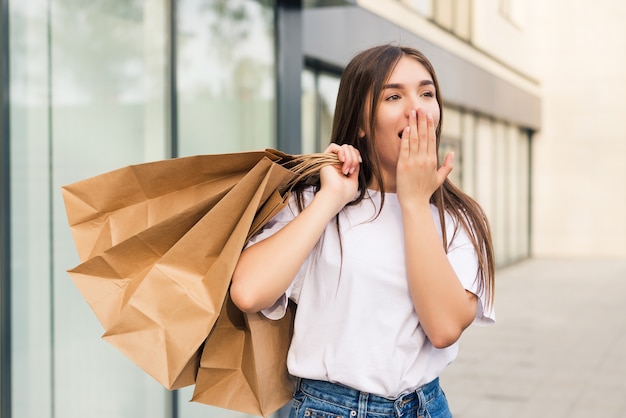 Verbaasde shopper die met boodschappentassen zijn mond opent en naar speciale aanbiedingen in winkels kijkt en op straat wijst