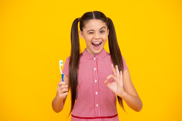 Verbaasde tiener Tienermeisje poetst haar tanden over geïsoleerde gele achtergrond Dagelijkse hygiëne tiener kind houd tandenborstel ochtendroutine Tandgezondheid mondverzorging Opgewonden tienermeisje