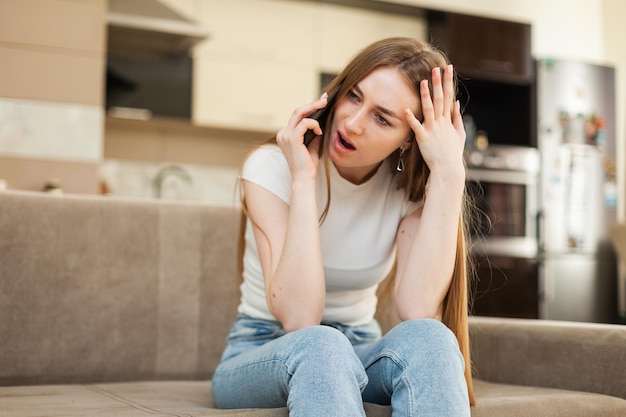 Verbaasde vrouw die aan de telefoon praat terwijl ze op de bank in de woonkamer zit