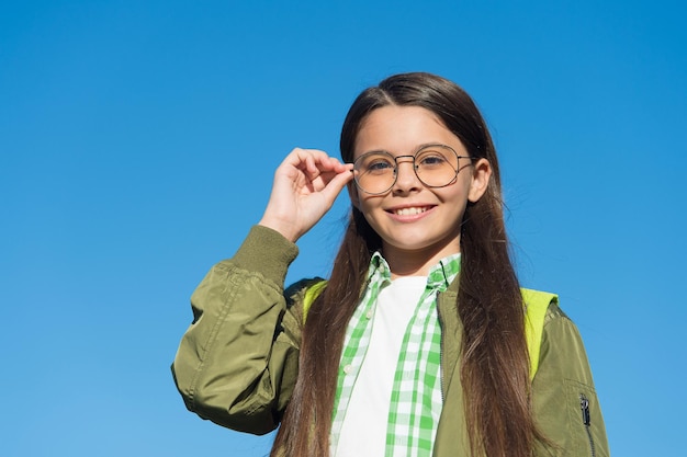 Verbeterd zicht is mogelijk. Gelukkig kind draagt een bril op zonnige blauwe hemel. Defecte visie. Visiecorrectie van kinderen. Corrigerende lens. Optische oogzorg. Oogheelkundige optica voor kinderen.
