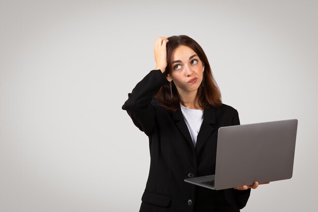 Verbijsterd jonge professionele vrouw met een laptop die haar hoofd krabt met een verbijsterde uitdrukking