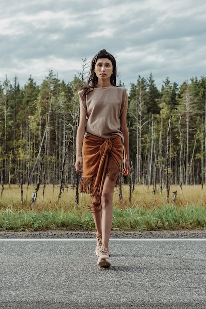 Verbluffende jonge Aziatische vrouw gekleed in een stijlvolle lokale outfit die de weg oversteekt in de buurt van het moerasbos