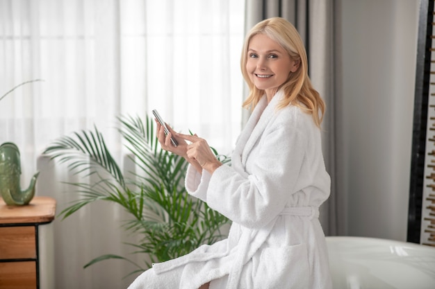 Verbonden. Een vrouw in een witte badjas met een smartphone in haar handen