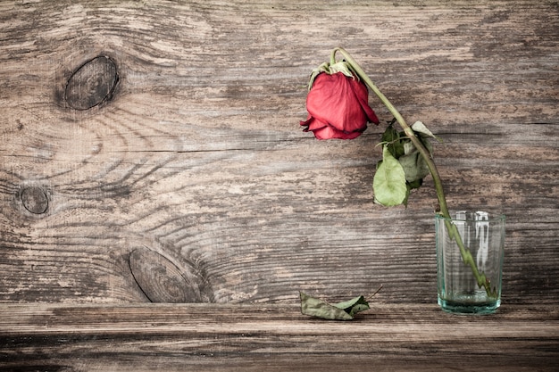 Verdorde gedroogde roos in glas op houten tafel