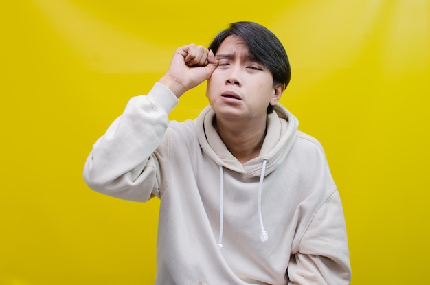 Foto verdrietig een jonge aziatische man met een grijs t-shirt met een huilende gezichtsuitdrukking is geïsoleerd op geel