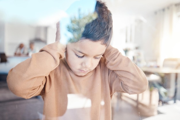 Verdrietig huis en jongen met handen op oren voor depressie angst en bang voor conflict met familie door raam Kinderpsychologie autisme en depressieve angst en overstuur kind in woonkamer voor geestelijke gezondheid