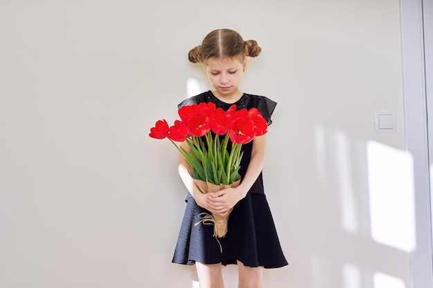 Verdrietig kindmeisje met een boeket rode tulpen in zwarte jurk