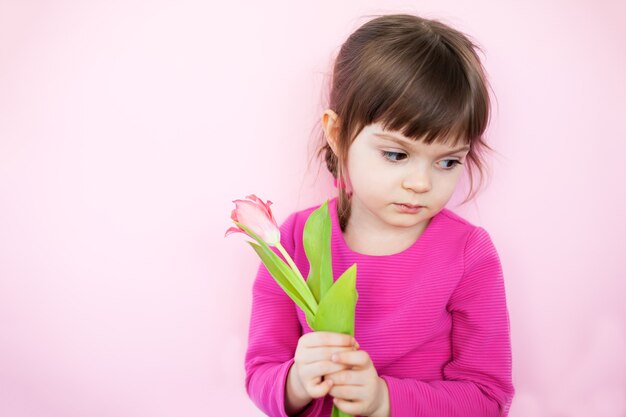 Verdrietig meisje in roze jurk met roze tulp