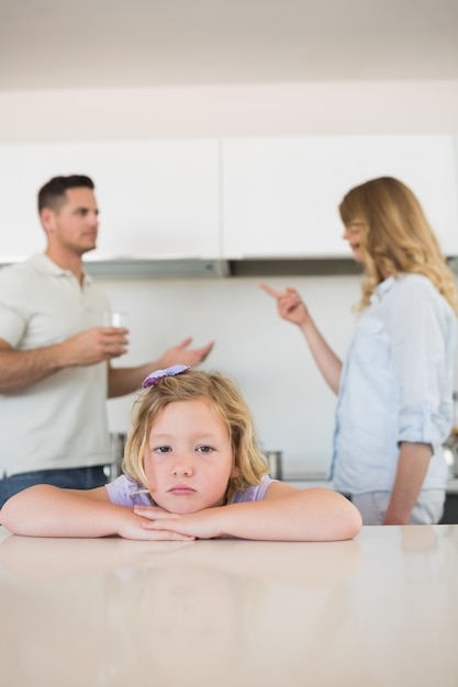 Verdrietig meisje leunend op tafel, terwijl ouders tegenstrijdig