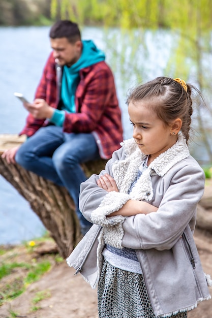 Verdrietig meisje omdat papa zijn telefoon checkt terwijl hij door het bos loopt en geen aandacht aan haar besteedt.