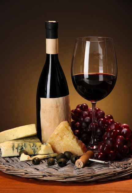 Verfijnd stilleven van wijn, kaas en druiven op rieten dienblad op houten tafel op bruine achtergrond