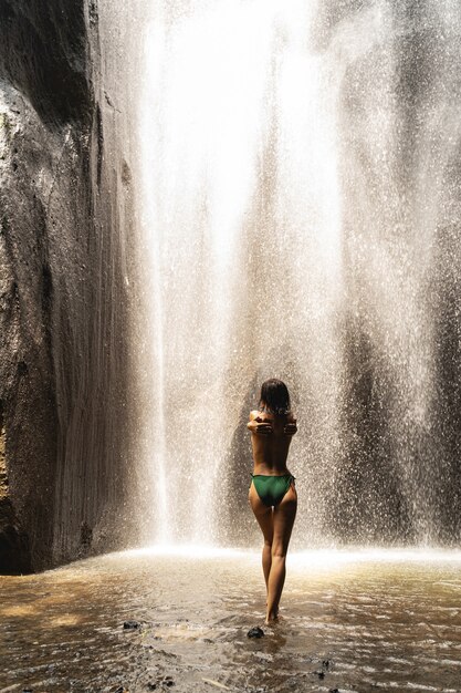 Verfris jezelf. Jonge brunette vrouwelijke persoon die voor de waterval staat en haar sportieve figuur laat zien