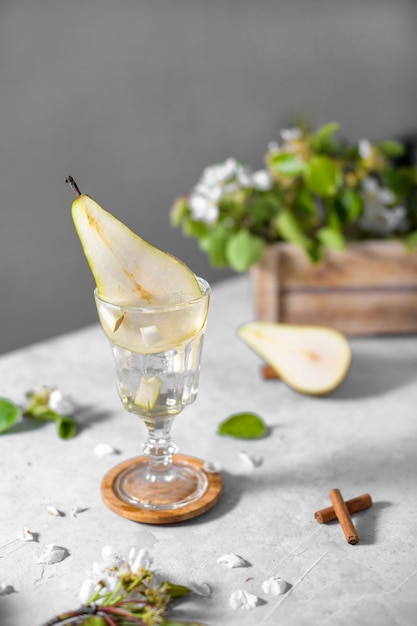 Verfrissende perencocktail in een glas versierd met vers fruit en bloemen op een lichtgrijze achtergrond Zomermocktail