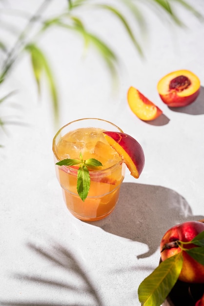 Foto verfrissende perzik thee met ijs en munt huisgemaakte koude gezonde vegetarische drank op een lichte achtergrond met vers fruit palmblad en schaduw