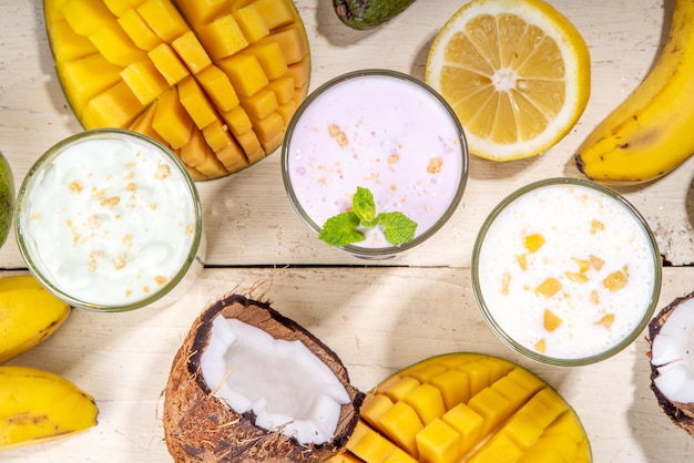 Verfrissende yoghurt milkshakes of smoothies Drie glazen met fruit milkshakes Witte banaan groene appel avocado gele mango tropische vruchten smoothie Op witte houten tafel kopie ruimte