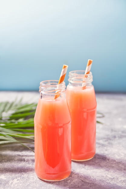 Verfrissende zomer tropische cocktail in een fles met rietje op een grijze betonnen tafel onder het palmblad.