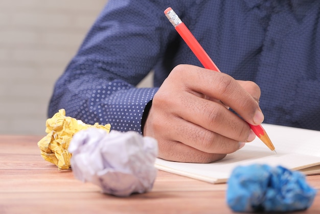 Verfrommeld papier bal en persoon schrijven op kladblok op houten tafel