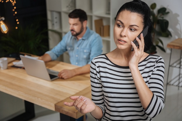 Vergaderarrangement. Aangename mooie aardige vrouw die een mobiele telefoon vasthoudt en een vergadering regelt terwijl ze voor haar baas werkt