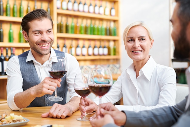 Vergadering van succesvolle cavists met glazen rode wijn aan tafel zitten en nieuwe soorten dranken bespreken