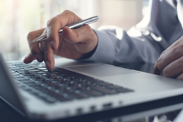 Vergaderverslag aan de gang Zakenman met pen in de hand typen op het toetsenbord van de laptopcomputer op bureau close-up