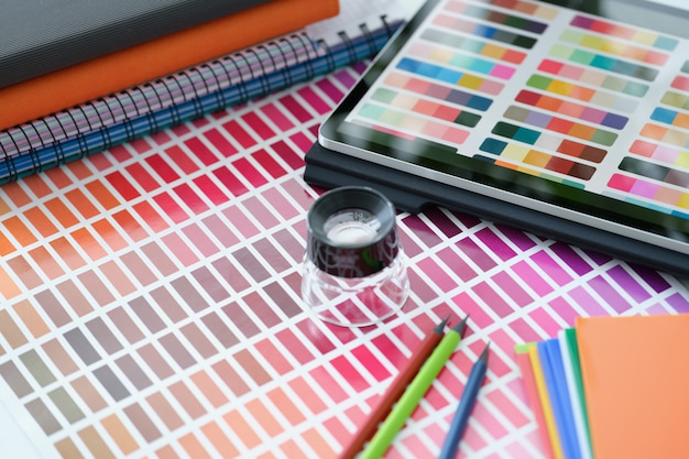 Vergrootglas liggend op papier met kleurstalen in de buurt van digitale tablet close-up kleurkwaliteit